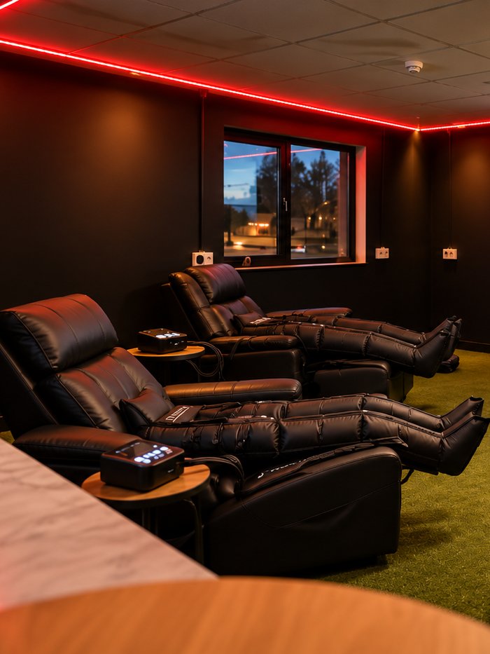 The recovery lounge at Baseline Recovery — leather recliners fitted with compression boots under red ceiling lighting